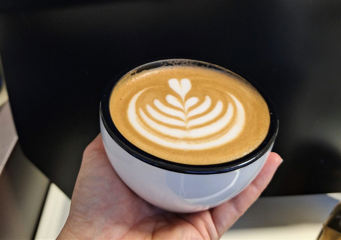 Cappuccino mit Rosetta in der Hand gehalten