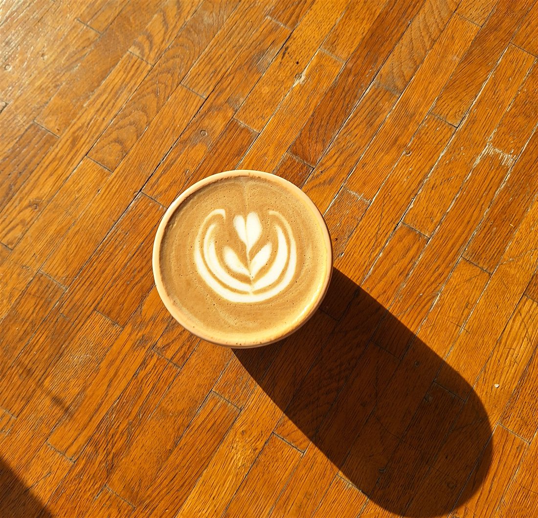 Flat White mit Tulpe auf Holzboden im Sonnenlicht