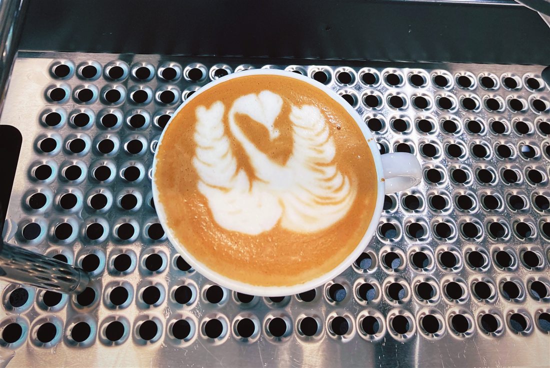 Latte Art Schwan in einer Tasse auf dem Abtropfblech der Siebträgermaschine